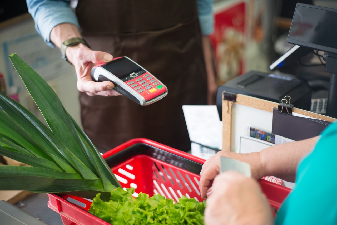 A customer using a contactless payment method at a grocery store checkout with fresh produce.